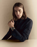 Person wearing a dark jacket and watch against a beige background