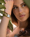 Woman wearing a gold Cartier watch with a blurred green leaf background